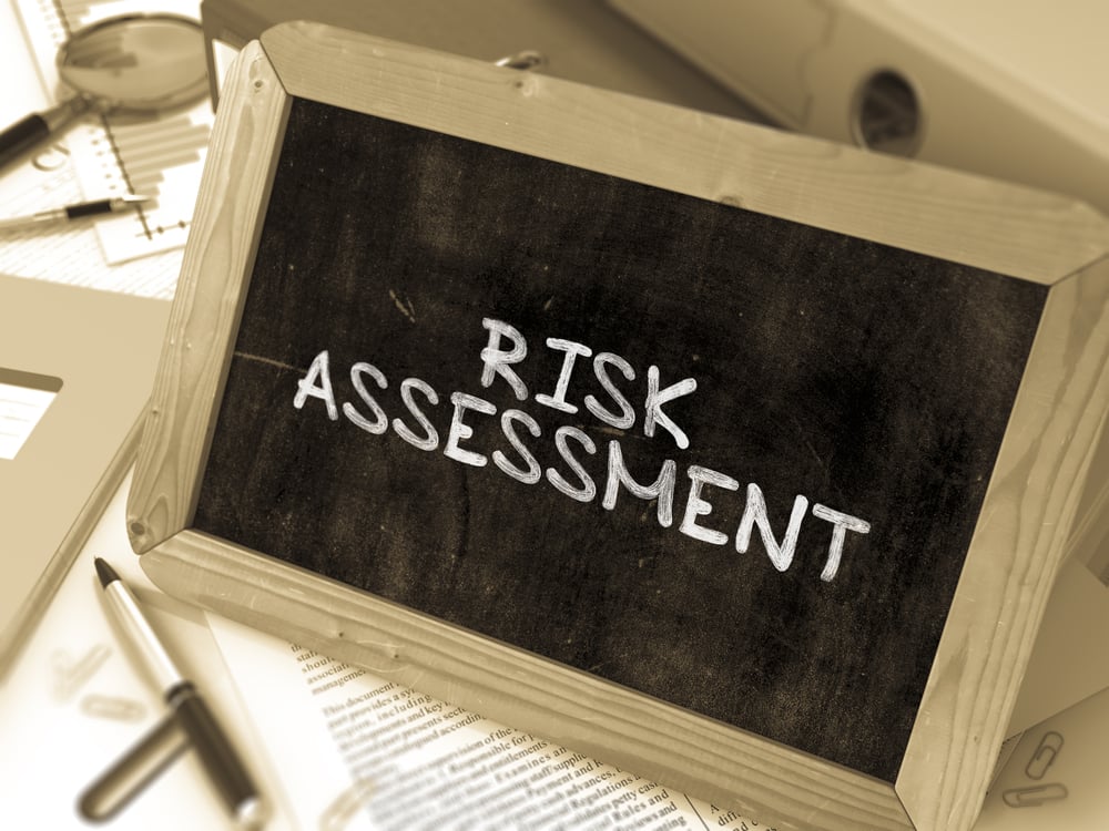 Handwritten Risk Assessment on a Chalkboard. Composition with Chalkboard and Ring Binders, Office Supplies, Reports on Blurred Background. Toned Image. 3D Render.